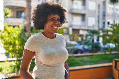 Afro-Amerikalı kadın gülümsüyor, parkın kenarına bakıyor.