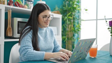 Genç İspanyol kadın yemek odasında dizüstü bilgisayar kullanıyor.