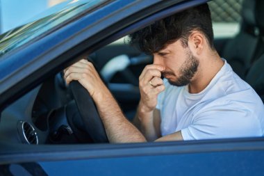 Young hispanic man driving car smelling bad smell at street clipart