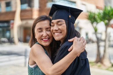 Two women mother and graduated daughter hugging each other at street