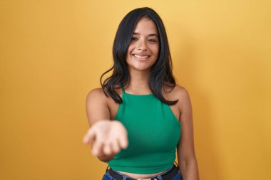 Sarı arka planda duran esmer kadın mutlu bir gülümsemeyle avuç içi yardım ve kabullenme teklif ediyor.. 