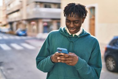 Sokakta akıllı telefon kullanan, kendinden emin gülümseyen Afrikalı Amerikalı bir adam.