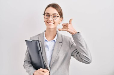 İş kıyafetleri ve gözlük takan, gülümseyen, el ve parmaklarıyla telefon hareketi yapan, telefonda konuşan beyaz bir kadın. iletişim kavramları. 