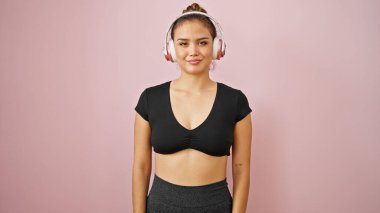 Genç ve güzel İspanyol kadın spor giyer. İzole edilmiş pembe arka planda müzik dinler.