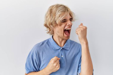 Soyutlanmış arka planda duran genç modern adam mutlu ve heyecanlı bir şekilde kollarını kaldırıp, gülümseyerek ve başarı için bağırarak kazanan bir jest yapıyor. kutlama konsepti. 