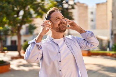 Parkta müzik dinlerken kendinden emin gülümseyen beyaz bir genç.