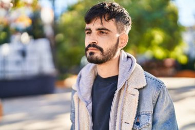Young hispanic man looking to the side with relaxed expression at park