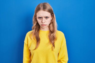 Mavi arka planda duran genç beyaz kadın şüpheci ve gergin, sorun yüzünden surat asıyor. negatif kişi. 