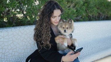 Köpekli genç İspanyol kadın parkta akıllı telefon kullanıyor.