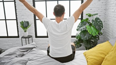 Gri saçlı, sabah erkenden uyanan, rahat yatak odasında kollarını rahatça açan, rahat bir aura ile odayı kutsayan olgun bir adamın iç açıcı görüntüsü.