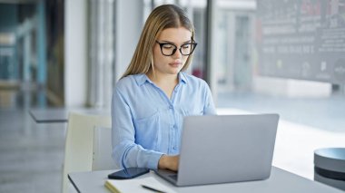 Ofiste çalışan genç sarışın iş kadını dizüstü bilgisayar kullanıyor.