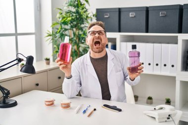 Orta yaşlı beyaz dişçi ağız gargargarası tutuyor kızgın ve kızgın bağırıyor sinirli ve öfkeli, öfkeyle bağırıyor.. 