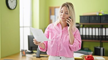 Genç sarışın iş kadını ofis telefonundan döküman okuyor.
