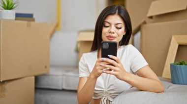 Young caucasian woman using smartphone sitting on floor at new home