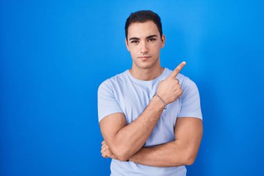 Mavi arka planda dikilen genç İspanyol adam, el ile işaret ederek reklamını yapıyor, ciddi ve sakin bir yüz ifadesi. 