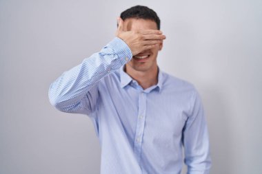 İş kıyafetleri ve gözlük takan yakışıklı İspanyol bir adam. Gülümsüyor ve elleri yüzünde, şaşırtmak için gözleri kapatıyordu. kör kavram. 