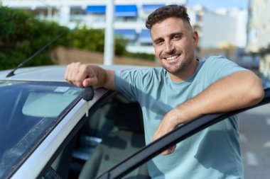 Young hispanic man smiling confident holding key of new car at street