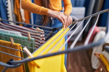 Young beautiful hispanic woman hanging clothes on clothesline at laundry room