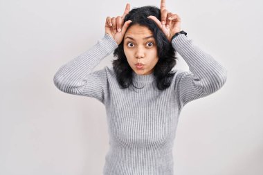 Koyu renk saçlı İspanyol bir kadın izole edilmiş arka planda duruyor ve parmağıyla boynuz şeklinde komik hareketler yapıyor. 