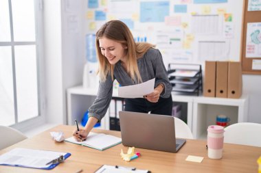 Ofisteki defterde yazan belgeleri okuyan genç sarışın iş kadını.