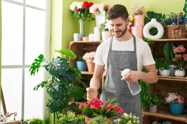 Genç beyaz erkek çiçekçi çiçekçide dağıtıcı sulama bitkisini kullanıyor.