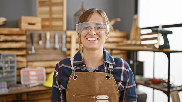 年轻的女木匠光彩夺目 一位漂亮的金发建筑工人自信地微笑在她的车间里 戴着安全眼镜站在那里 拥有木工游戏 — 图库照片