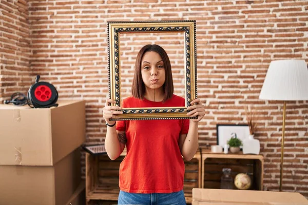 Young Hispanic Woman New Home Holding Empty Frame Puffing Cheeks — Stock Photo, Image
