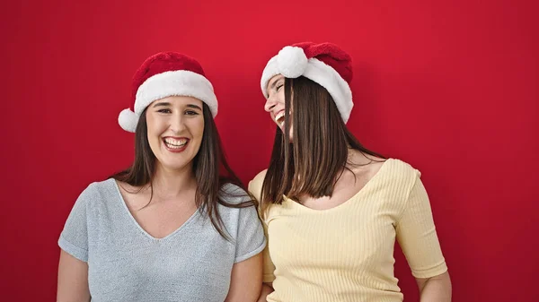 Dvě Ženy Usmívají Sebevědomě Nosí Vánoční Klobouk Přes Izolované Červené — Stock fotografie