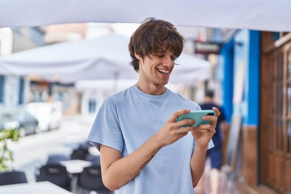 Young blond man smiling confident watching on smartphone at street