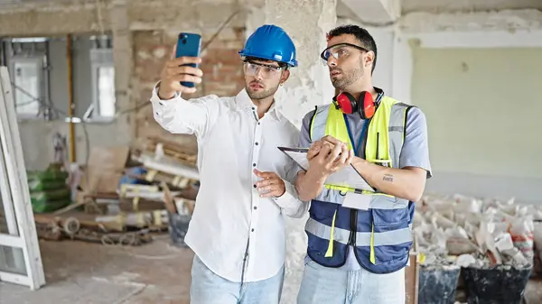 Two men builders and architect having video call writing on document at construction site