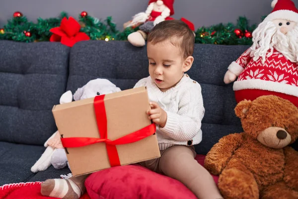 家でソファーに座っているクリスマスの贈り物を荷を下ろす愛らしいヒスパニックの幼児 — ストック写真