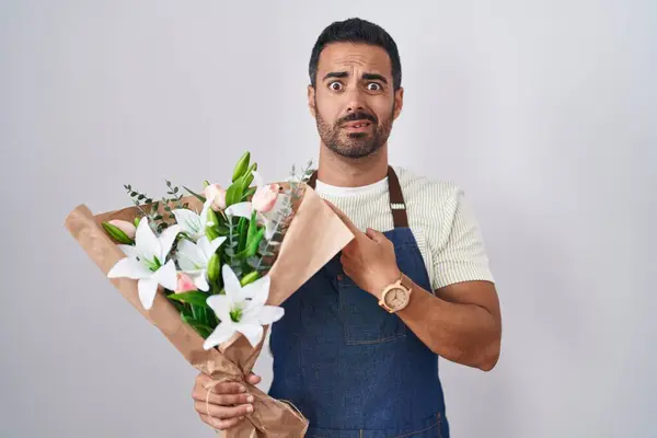 Hispanic man with beard working as florist pointing aside worried and nervous with forefinger, concerned and surprised expression