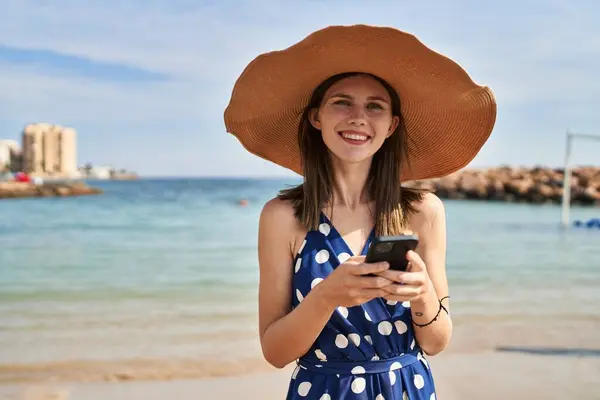 海滩上戴着夏帽 头戴智能手机的金发女游客 — 图库照片