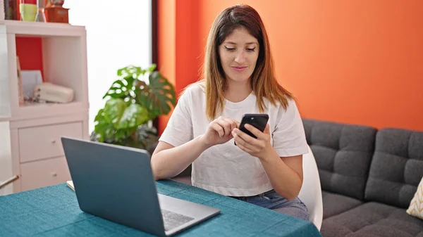 Genç Sarışın Kadın Yemek Odasında Akıllı Telefon Laptop Kullanıyor — Stok fotoğraf