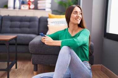 Genç ve güzel İspanyol kadın akıllı telefon kullanıyor. Evde yerde oturuyor.