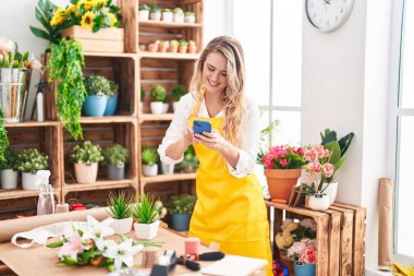 Çiçekçiye akıllı telefon kullanarak gülümseyen genç sarışın kadın.