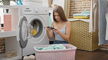 Çamaşır odasında video oyunu oynayan güzel bir kız çamaşır yıkıyor.