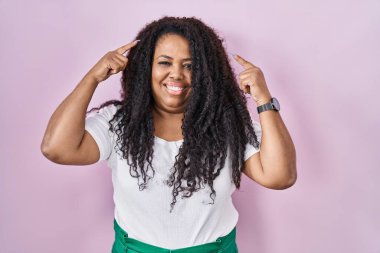 Artı, pembe arka planda duran İspanyol kadın gülümsemesi iki eliyle başını işaret ediyor, harika bir fikir ya da düşünce, iyi bir hafıza. 