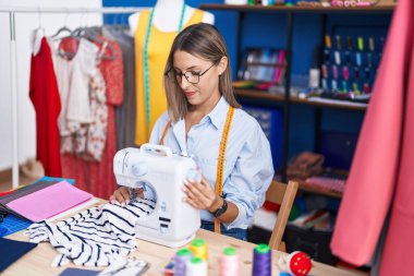 Elbise fabrikasında dikiş makinesi kullandığından emin bir şekilde gülümseyen güzel İspanyol kadın.