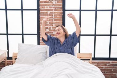 Orta yaşlı bir kadın yatak odasında kollarını açarak uyanıyor.