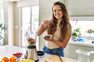 Genç, güzel İspanyol kadın mutfakta sebze suyu ve blender hazırlıyor.
