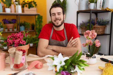 Çiçekçide çalışan İspanyol asıllı genç adam kollarını kavuşturup kameraya bakarken gülümsüyor. pozitif kişi. 