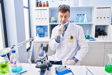 Laboratuvarda çalışan beyaz bir adam şüphe üzerine yoğunlaşmıştı. Parmakları çenesinde ve yukarı bakıyordu. 