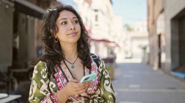 Genç ve güzel İspanyol kadın akıllı telefon kullanıyor. Sokakta ciddi bir ifadesi var.