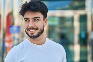 Young hispanic man smiling confident looking to the side at street