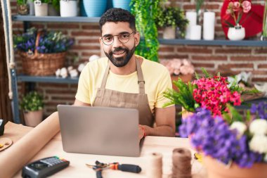 Young arab man florist smiling confident using laptop at florist