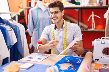 Young hispanic man tailor showing clothing design speaking at atelier