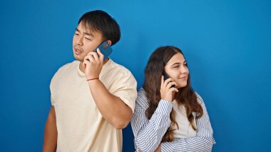 Kadın ve erkek, gülümseyen, kendine güvenen, mavi arka planda akıllı telefonlardan konuşan çift.