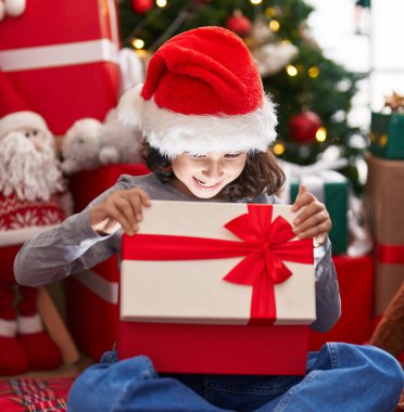 Sevimli Çinli kız hediyesini açıyor. Noel ağacının yanında oturuyor.