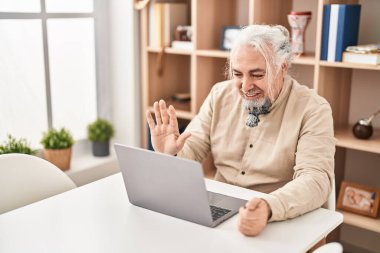 Middle age grey-haired man having video call sitting on table at home